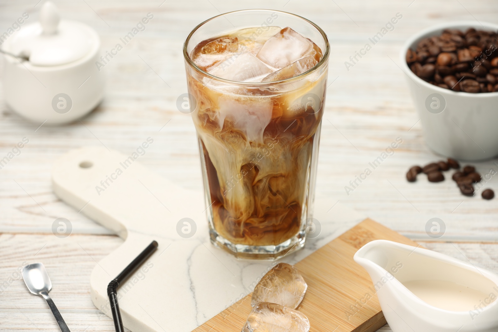 Photo of Refreshing iced coffee with milk in glass and beans on white wooden table, closeup