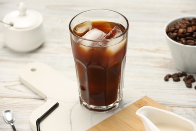 Photo of Refreshing iced coffee in glass and beans on white wooden table, closeup