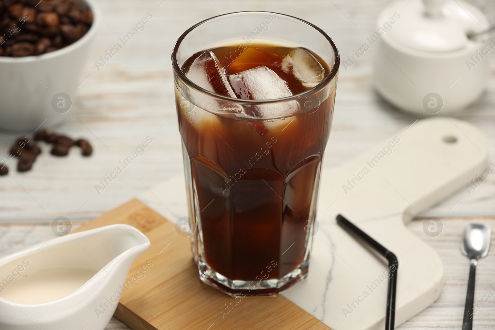 Photo of Refreshing iced coffee in glass and beans on white wooden table, closeup