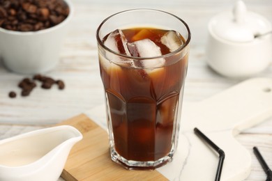 Photo of Refreshing iced coffee in glass and beans on white wooden table, closeup