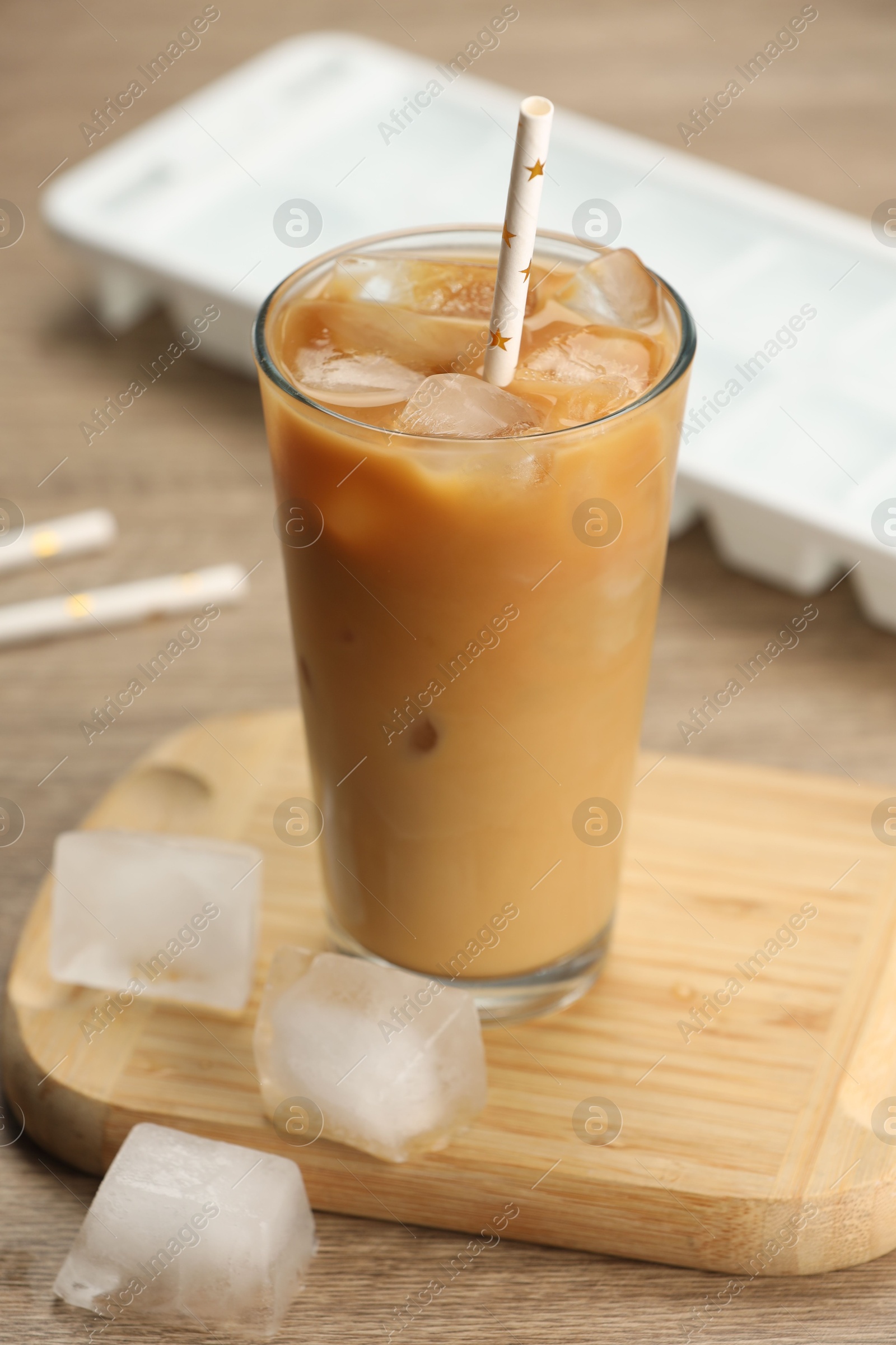 Photo of Refreshing coffee with ice and milk in glass on wooden table, closeup