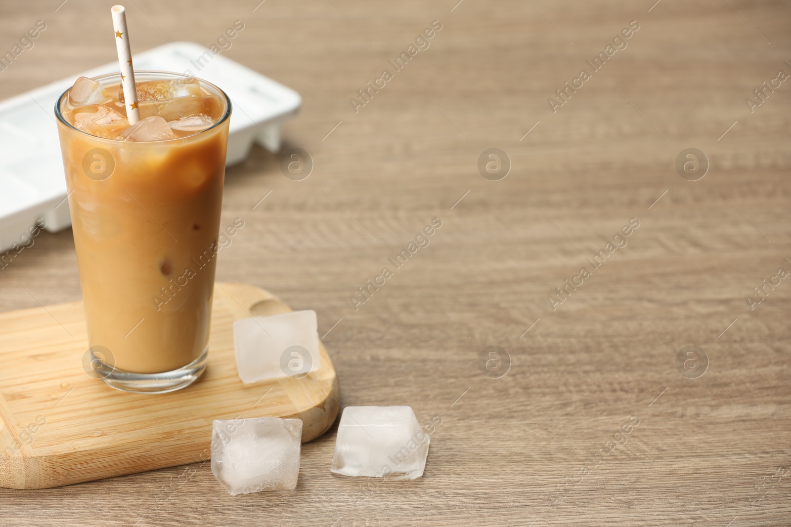 Photo of Refreshing coffee with ice and milk in glass on wooden table. Space for text