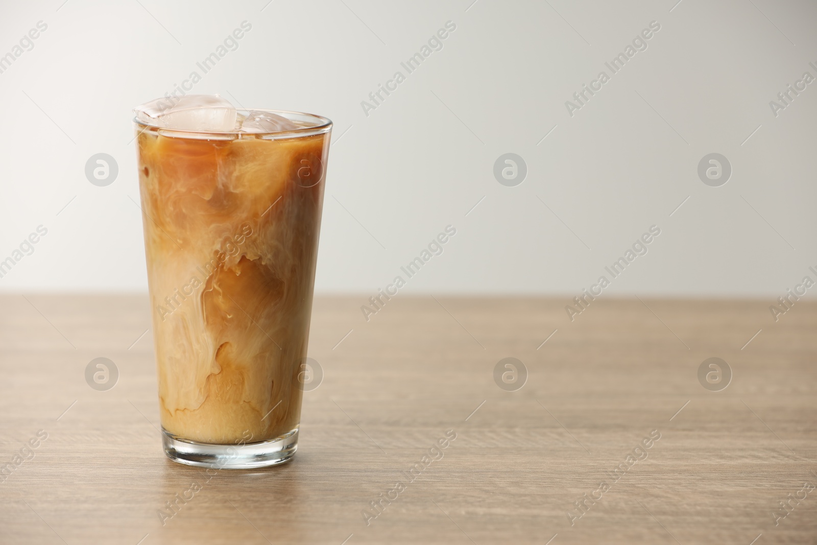 Photo of Refreshing iced coffee with milk in glass on wooden table against light background. Space for text