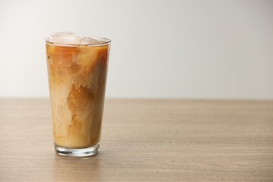 Photo of Refreshing iced coffee with milk in glass on wooden table against light background. Space for text