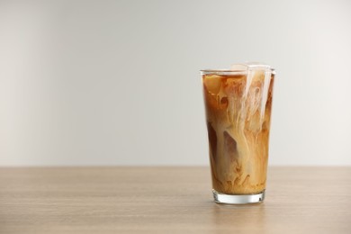 Photo of Refreshing iced coffee with milk in glass on wooden table against light background. Space for text