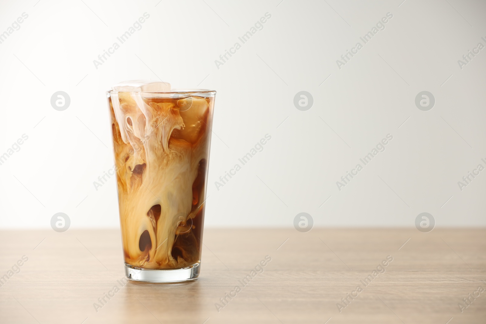 Photo of Refreshing iced coffee with milk in glass on wooden table against light background. Space for text