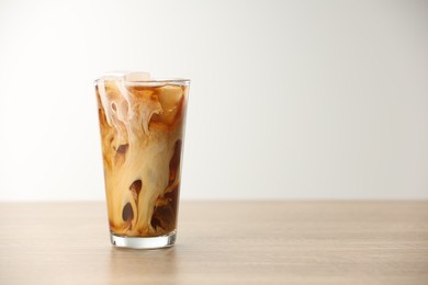 Photo of Refreshing iced coffee with milk in glass on wooden table against light background. Space for text