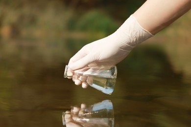 Photo of Examination of water quality. Researcher taking water sample from lake outdoors, closeup