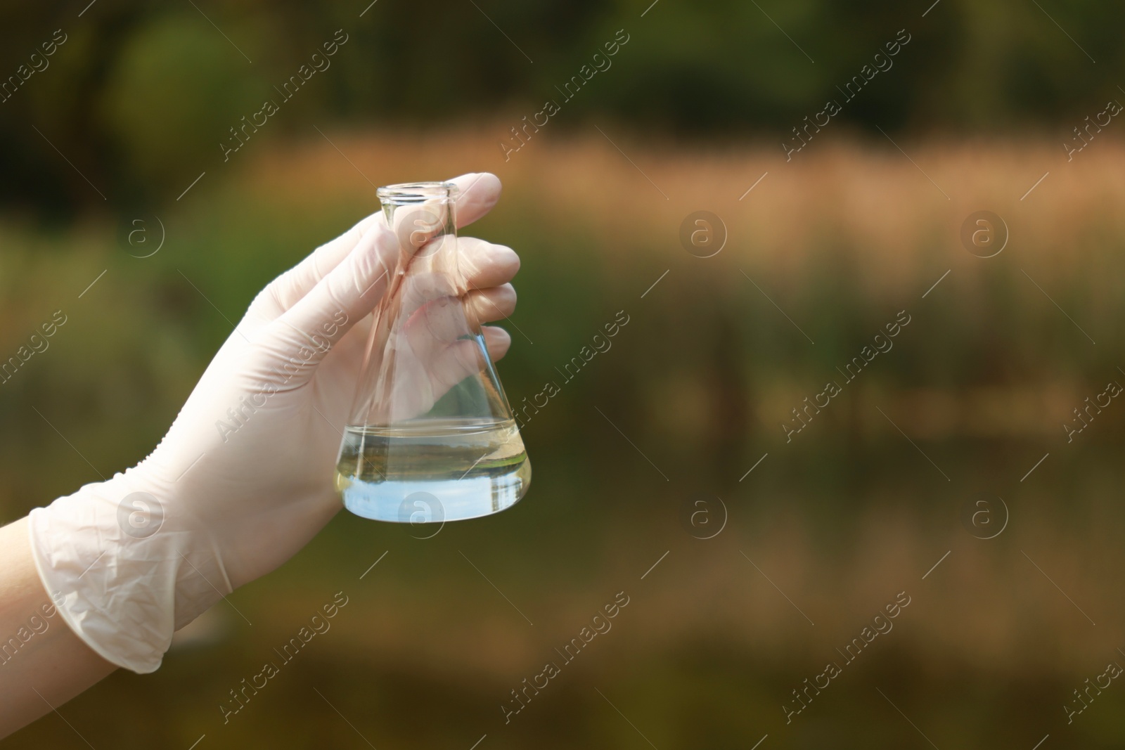 Photo of Examination of water quality. Researcher holding flask with sample outdoors, closeup. Space for text