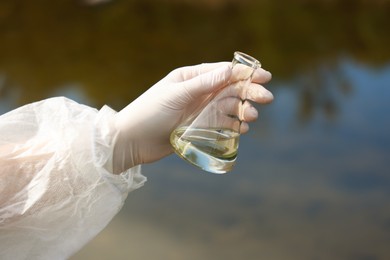 Photo of Examination of water quality. Researcher holding flask with sample outdoors, closeup