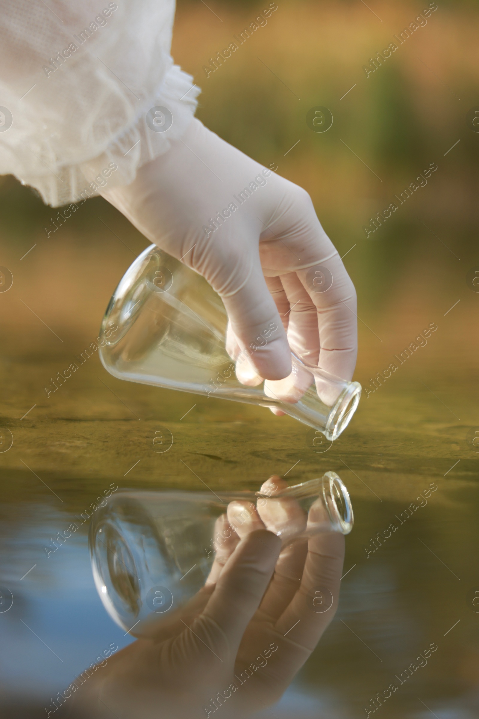 Photo of Examination of water quality. Researcher taking water sample from lake outdoors, closeup