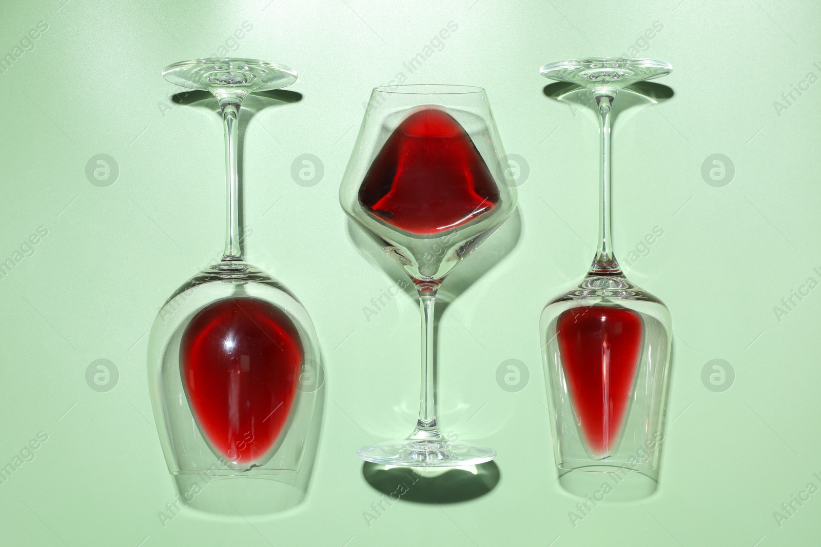 Photo of Glasses of red wine on light green background, flat lay