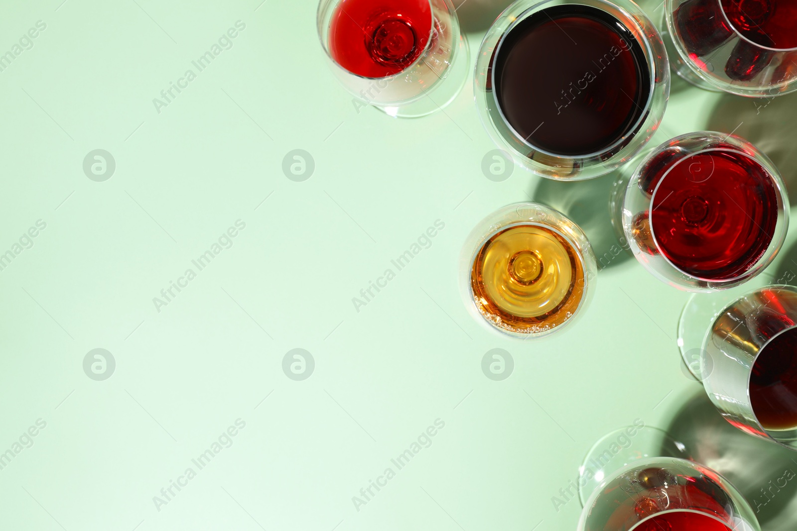 Photo of Glasses of different drinks on light green background, flat lay. Space for text