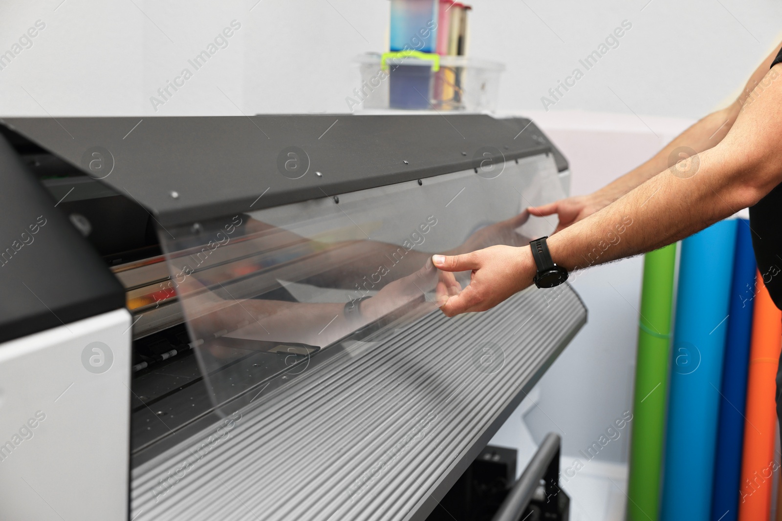 Photo of Man using wide-format printer indoors, closeup. Printing house