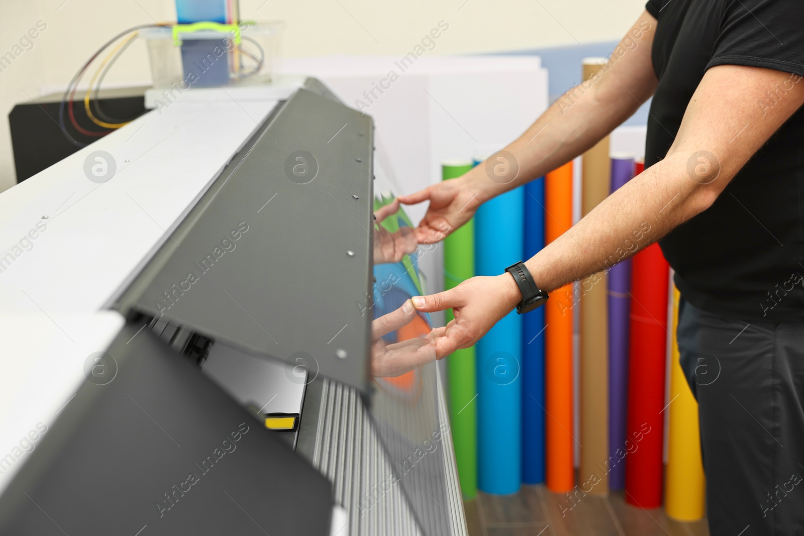 Photo of Man using wide-format printer indoors, closeup. Printing house