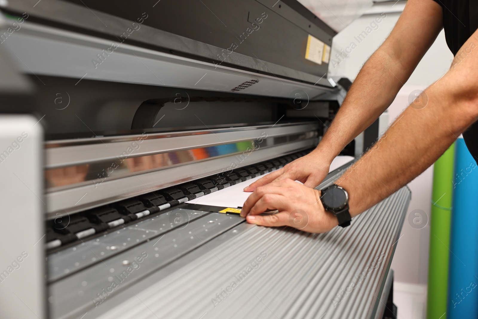 Photo of Man using wide-format printer indoors, closeup. Printing house