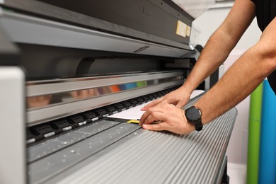 Photo of Man using wide-format printer indoors, closeup. Printing house