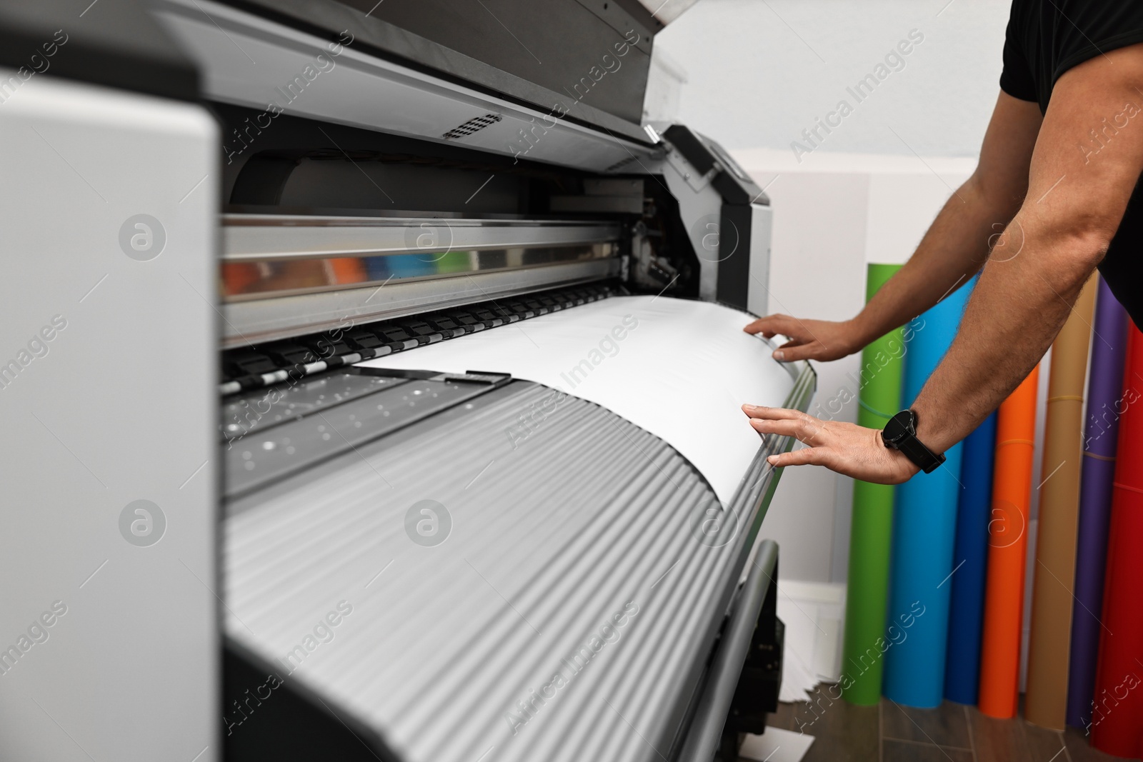 Photo of Man using wide-format printer indoors, closeup. Printing house