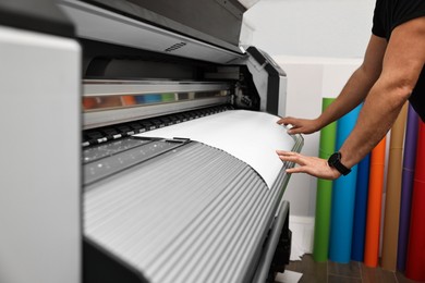 Photo of Man using wide-format printer indoors, closeup. Printing house