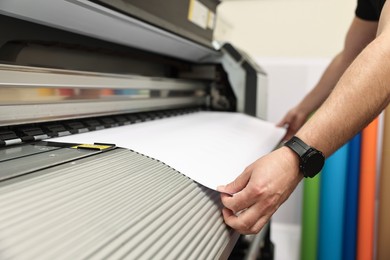 Photo of Man using wide-format printer indoors, closeup. Printing house