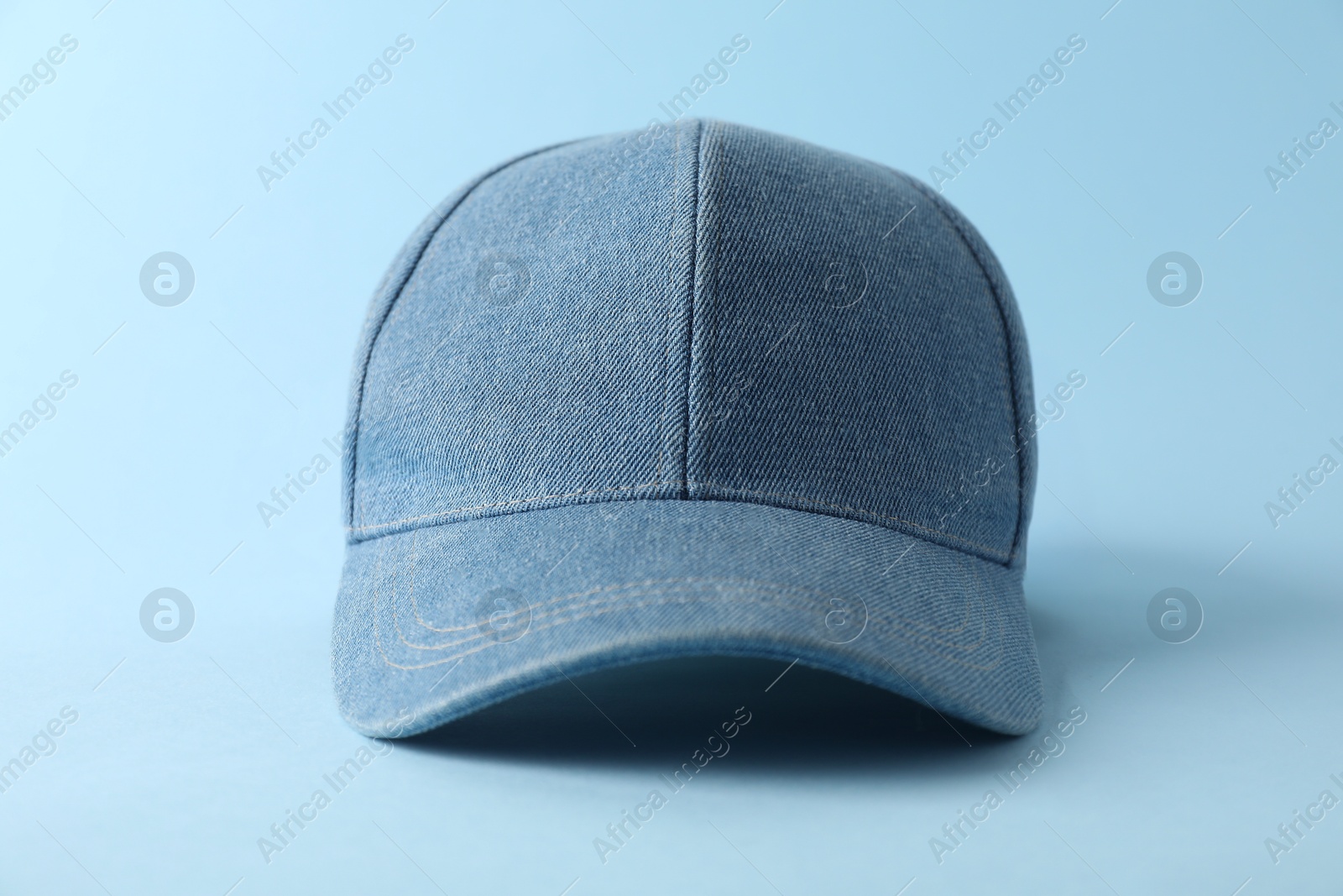 Photo of Stylish denim baseball cap on light blue background, closeup. Mockup for design