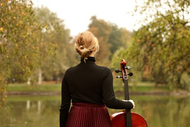 Photo of Woman with cello in park, back view. Classic musical instrument