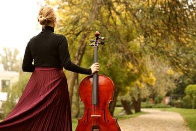 Photo of Woman with cello in park, back view. Space for text