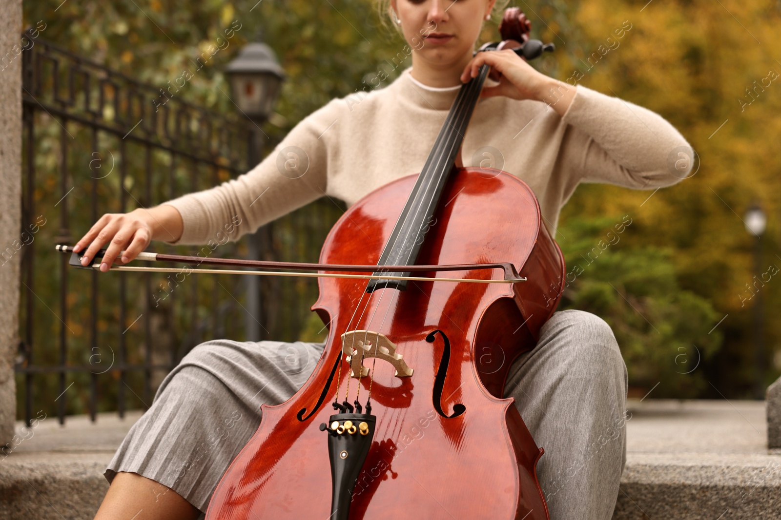 Photo of Young woman playing cello on stairs outdoors, closeup. Classic musical instrument