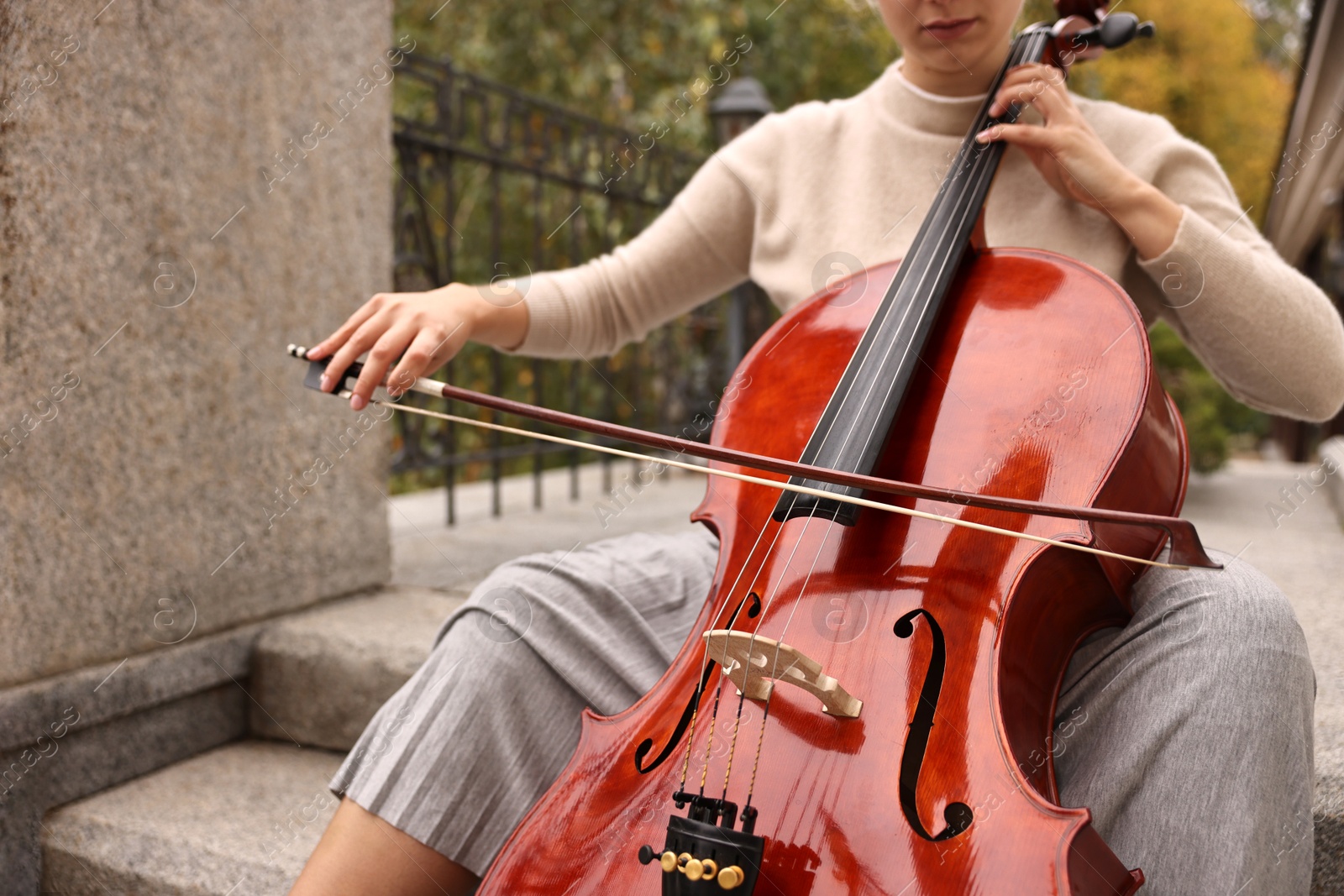 Photo of Young woman playing cello on stairs outdoors, closeup. Classic musical instrument