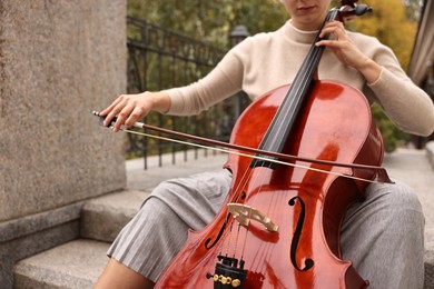 Photo of Young woman playing cello on stairs outdoors, closeup. Classic musical instrument