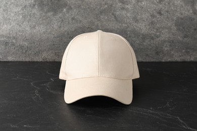 Photo of Stylish baseball cap on dark textured table. Mockup for design