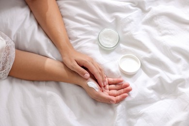 Photo of Woman applying cream onto hand on bed at home, top view