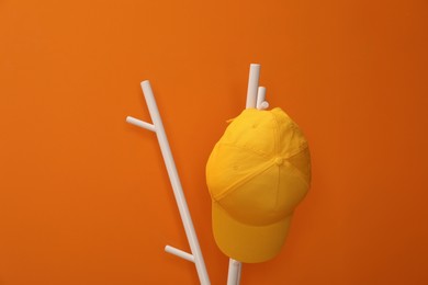 Photo of Stylish baseball cap on coat rack against orange wall. Mockup for design