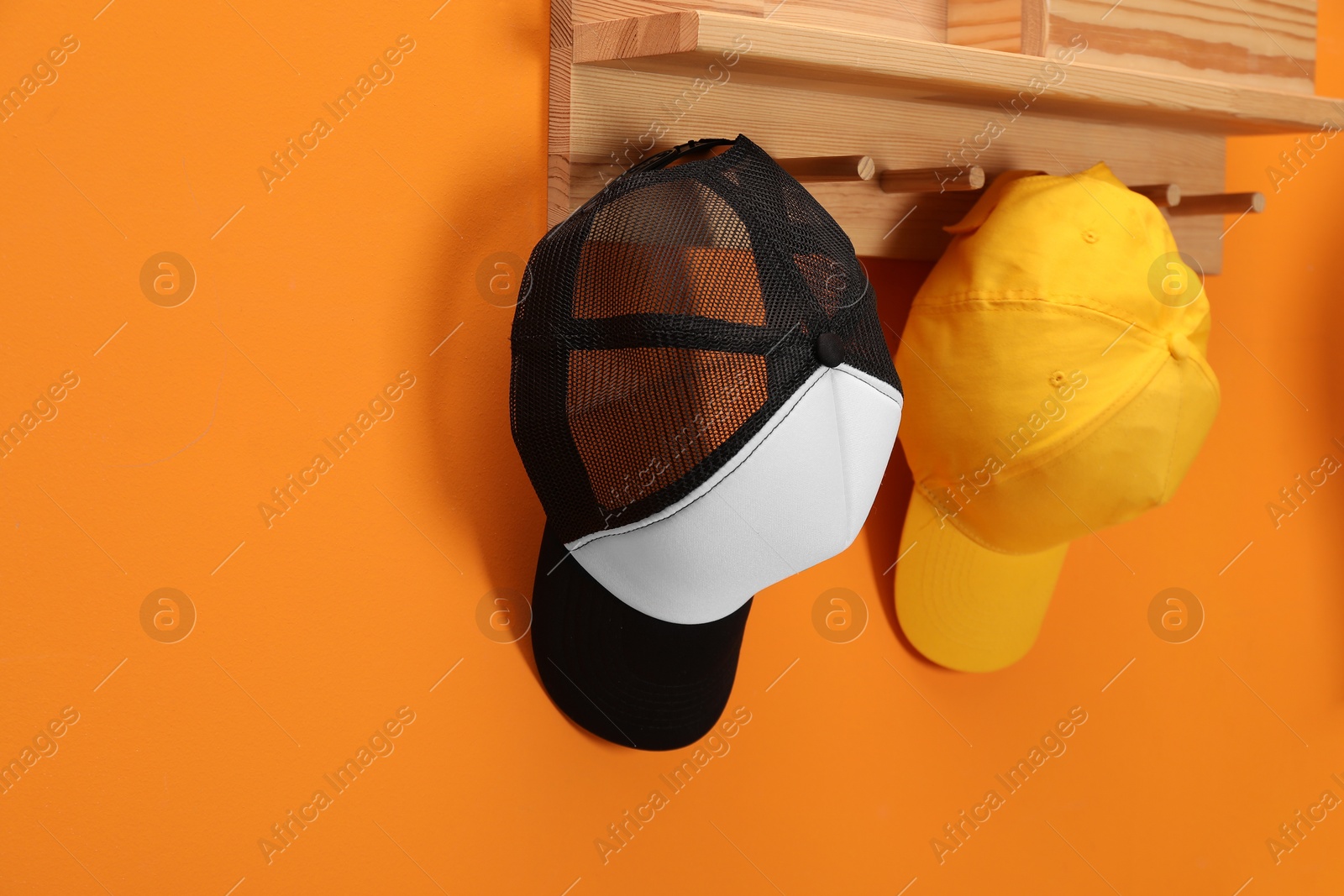 Photo of Stylish baseball caps on orange wall. Mockup for design