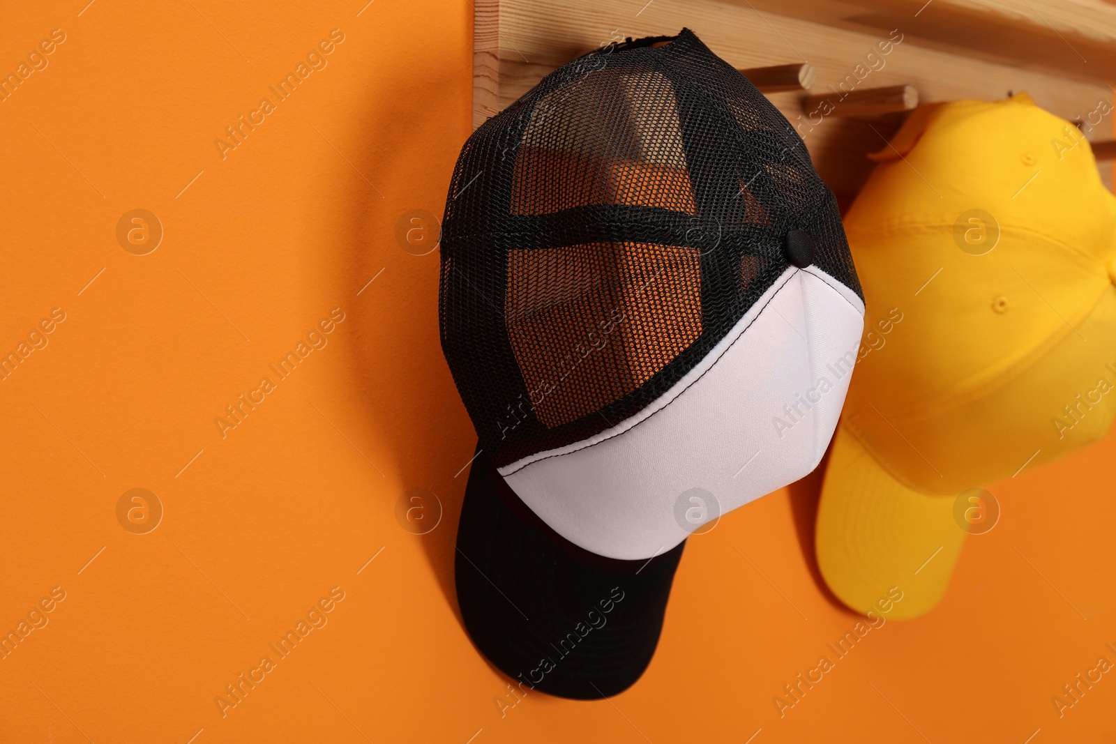 Photo of Stylish baseball caps on orange wall. Mockup for design