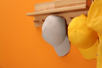 Photo of Stylish baseball caps on orange wall. Mockup for design