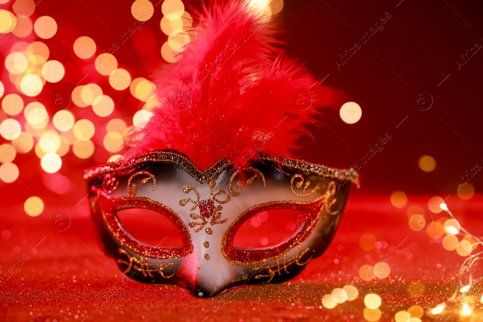 Photo of Beautiful carnival mask on shiny red background, closeup. Bokeh effect