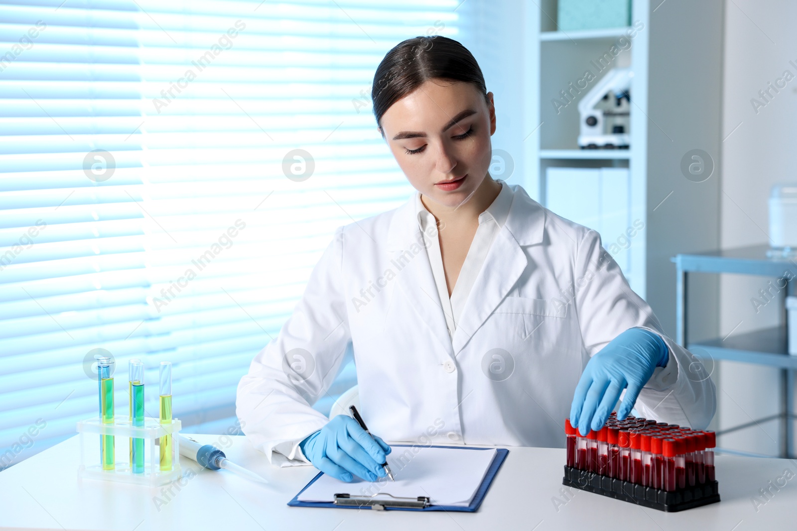 Photo of Laboratory testing. Doctor taking test tube with blood sample while working at table indoors