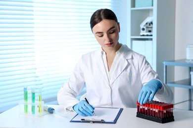 Photo of Laboratory testing. Doctor taking test tube with blood sample while working at table indoors