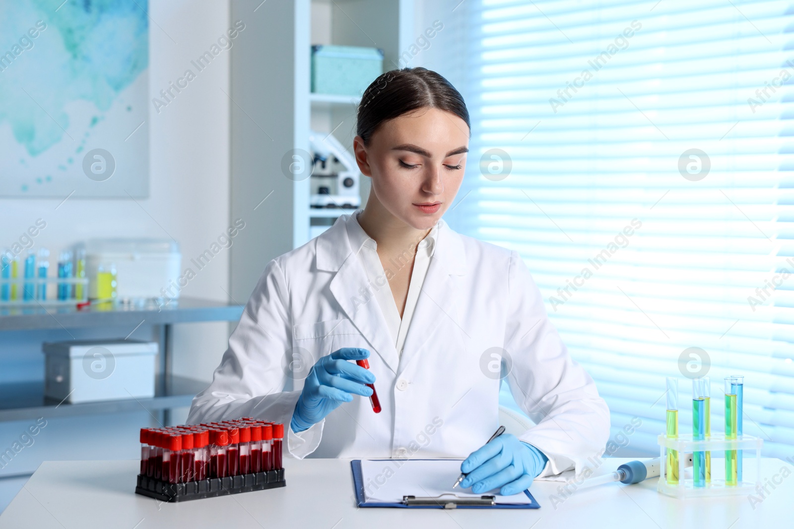 Photo of Laboratory testing. Doctor with blood sample taking notes at table indoors