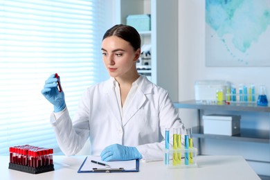 Photo of Laboratory testing. Doctor holding test tube with blood sample at table indoors