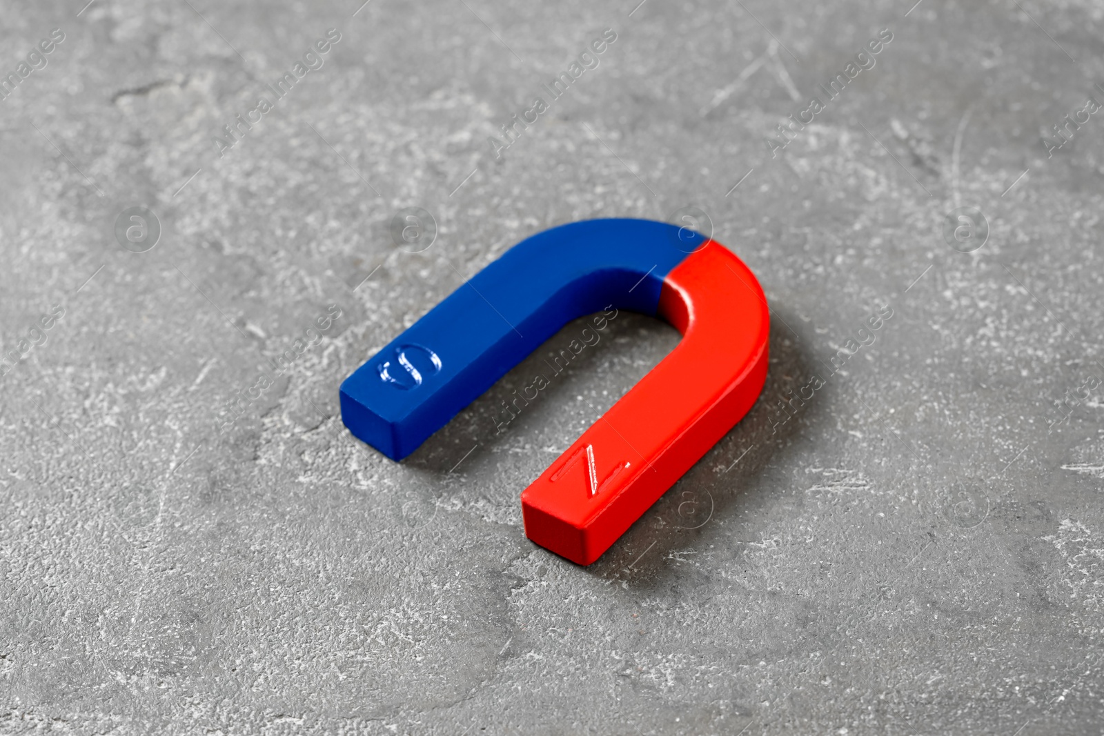 Photo of One horseshoe magnet on grey textured table, closeup