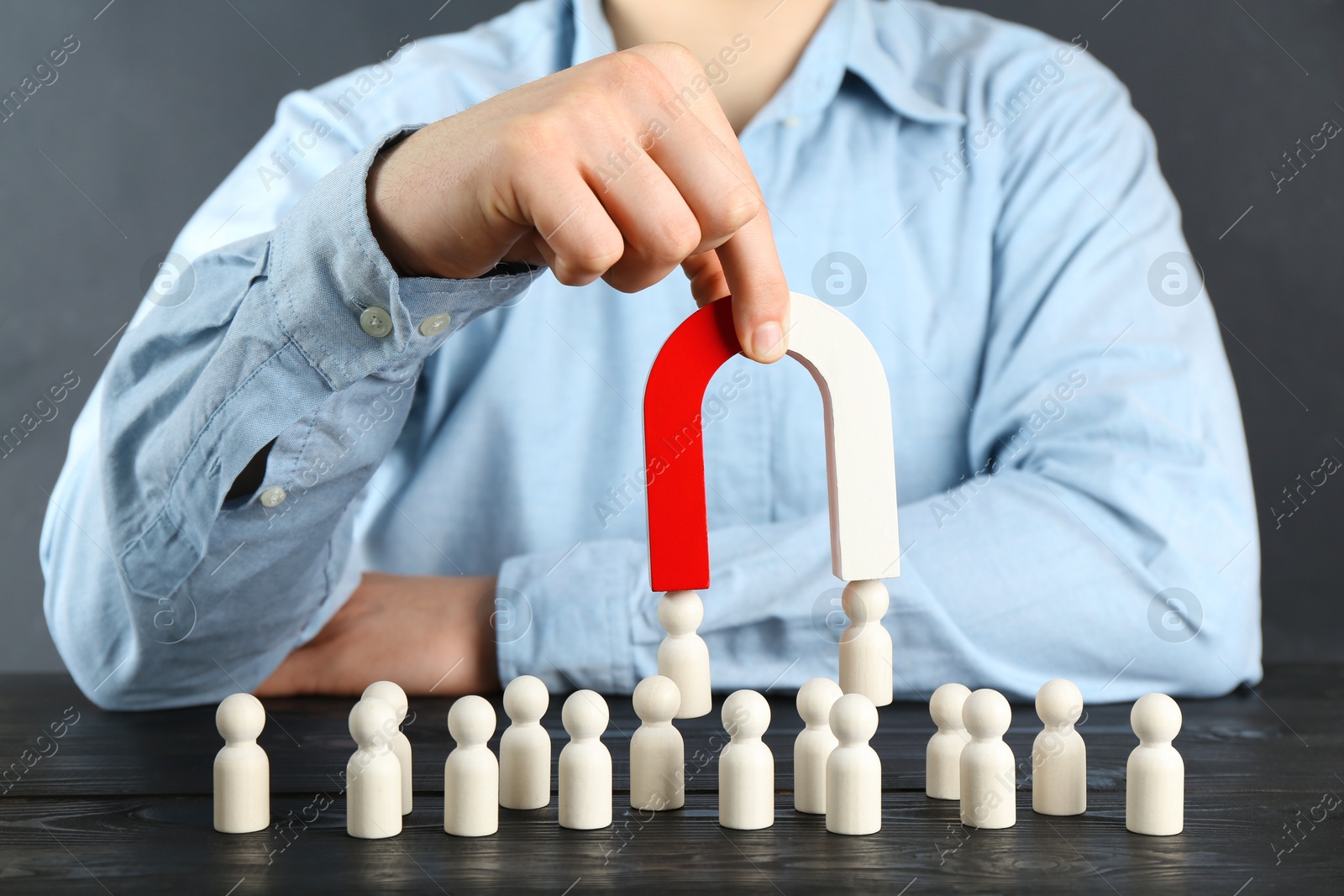 Photo of Man with magnet attracting human figures at black wooden table, closeup