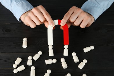 Photo of Man with magnet attracting human figures at black wooden table, closeup