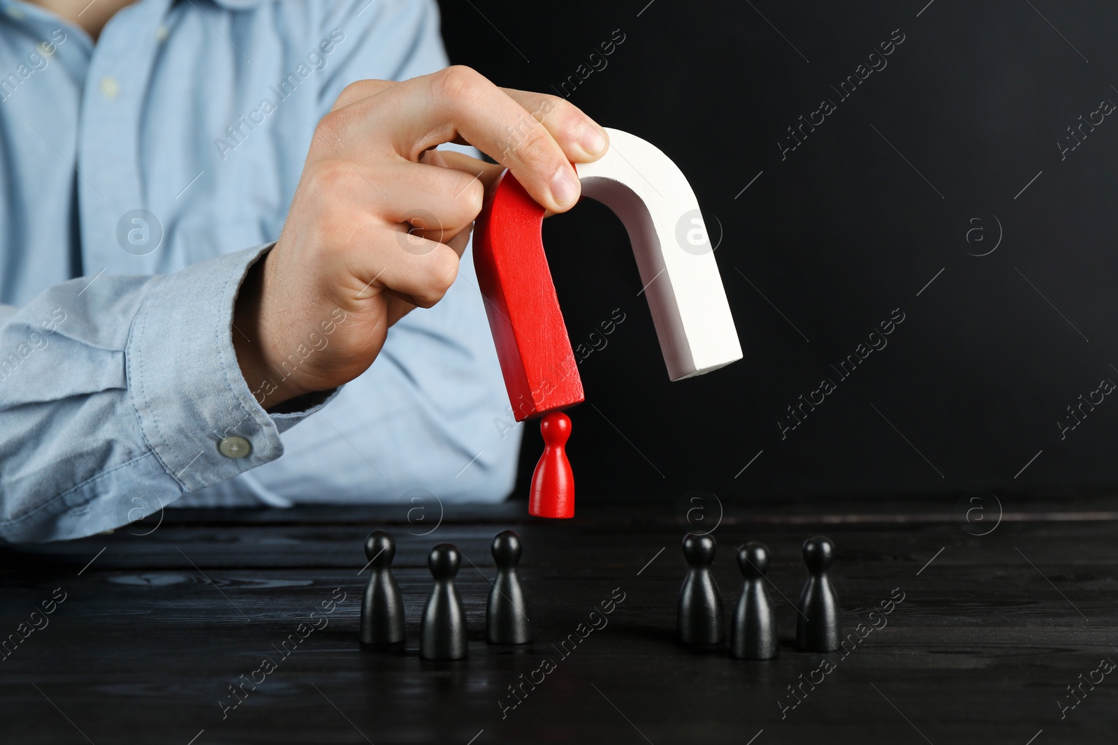 Photo of Man with magnet attracting red piece among black ones at wooden table, closeup