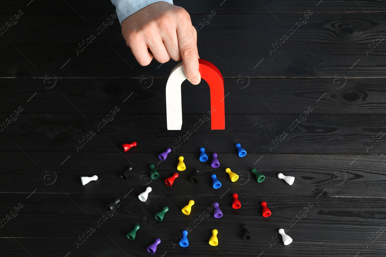 Photo of Man with magnet attracting different colorful game pieces at black wooden table, above view