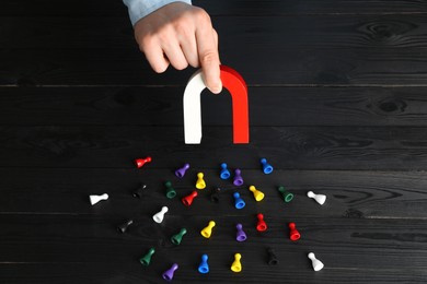 Photo of Man with magnet attracting different colorful game pieces at black wooden table, above view