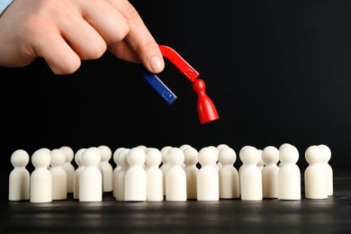 Photo of Man with magnet attracting red piece among wooden ones at black table, closeup