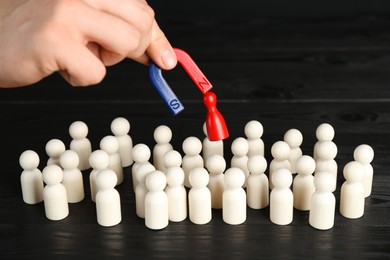 Photo of Man with magnet attracting red piece among wooden ones at black table, closeup