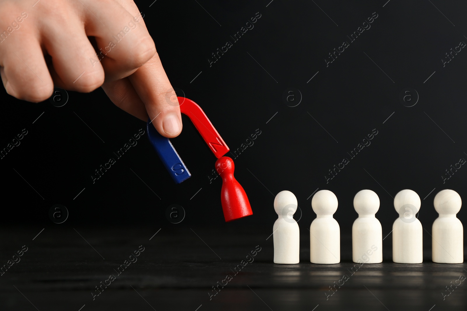 Photo of Man with magnet attracting red piece among wooden ones at black table, closeup